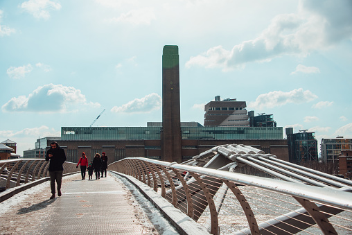 London, England - 28 February 2018: Some people crossing Millennium Bridge, while Tate Modern building can be seen on the other side of the Thames river.