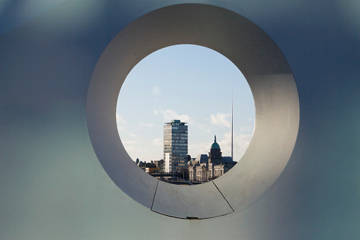 View of the Dublin City Centre through a hole in a sculpture. Liberty Hall, The Customs House and the Spire are all visible.