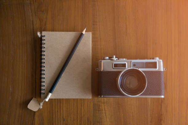 Retro camera with notebook and pencil by flat lay phot; flare light from window