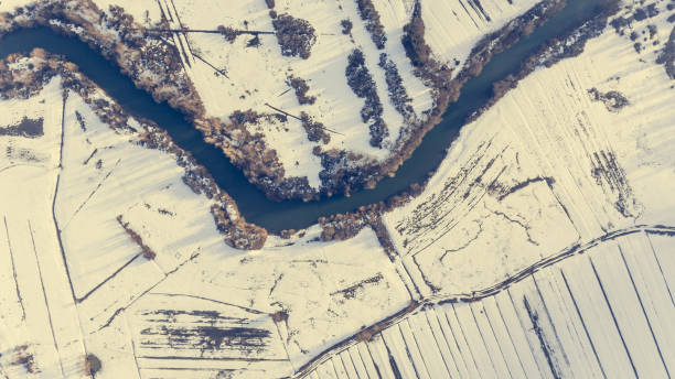 Aerial view riverbend passing snow covered fields. Drop down photography.