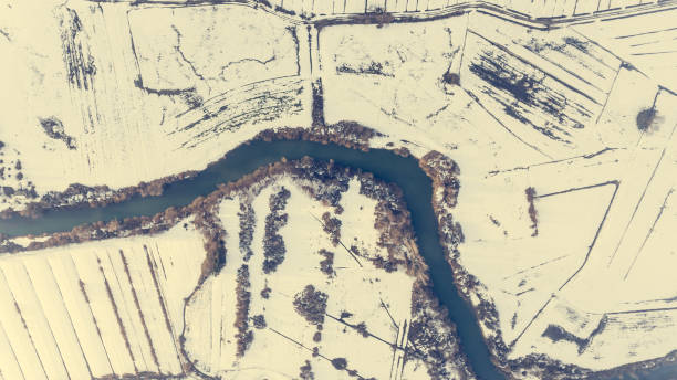 Aerial view riverbend passing snow covered fields. Drop down photography.
