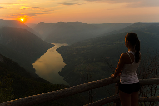 Young woman enjoying view at the top of the mountain at summer sunrise.