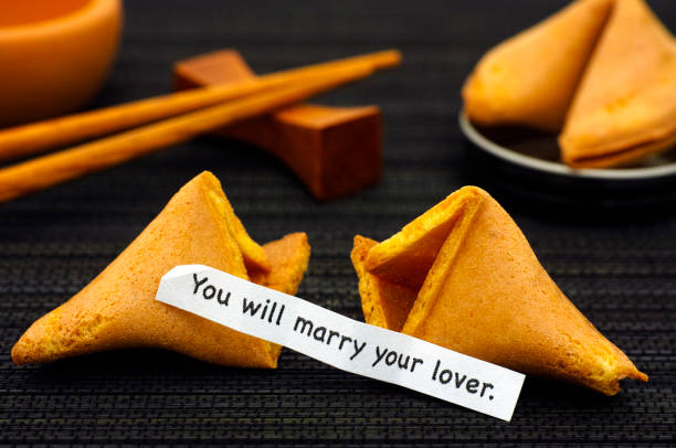 istock Paper strip with phrase You Will Marry Your Lover from fortune cookie, another cookie and chopsticks on black napkin background. 931480558