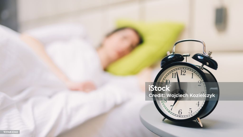 Jovem mulher dormindo e despertador no quarto em casa - raso profundidade de campo - Foto de stock de Acordar royalty-free