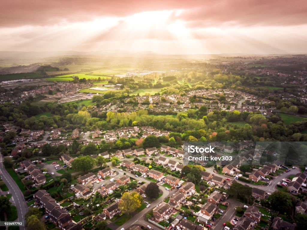 Sun bursting through clouds over traditional British houses with countryside in the background. Dramatic lighting and warm colours to give a homely effect. Community Stock Photo