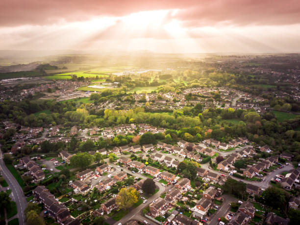 Sun bursting through clouds over traditional British houses with countryside in the background. Dramatic lighting and warm colours to give a homely effect. house uk countryside stock pictures, royalty-free photos & images