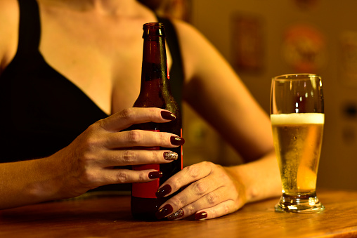 Closeup of a woman's hands holding a bottle of beer next to a full glass