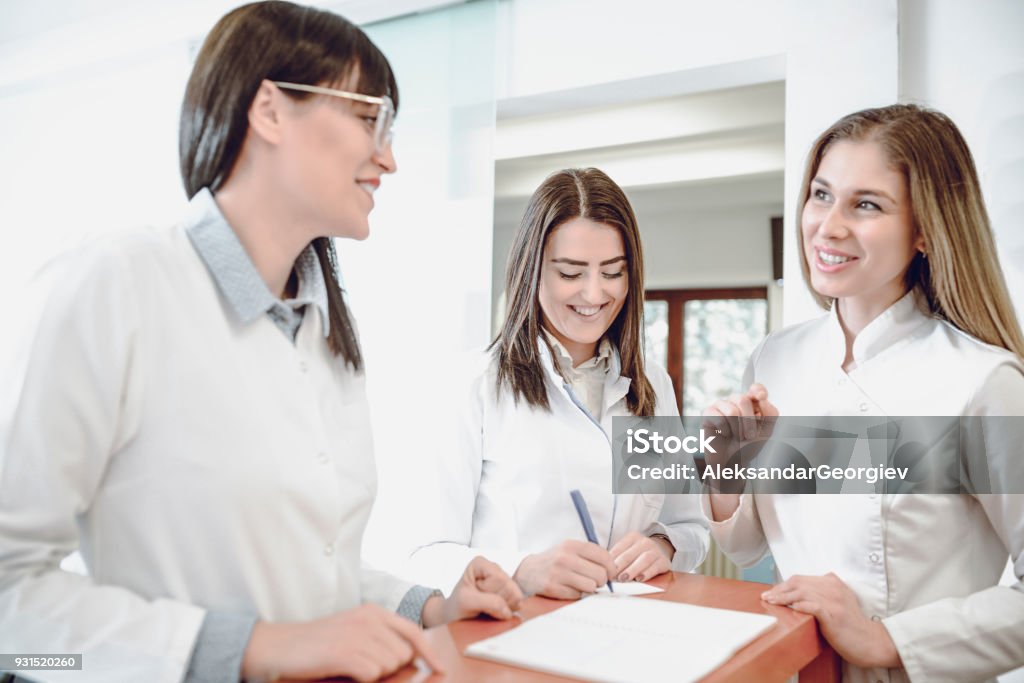 Gruppe von lächelnden junge Ärztinnen im Gespräch an der Rezeption in Klinik - Lizenzfrei Zusammenarbeit Stock-Foto