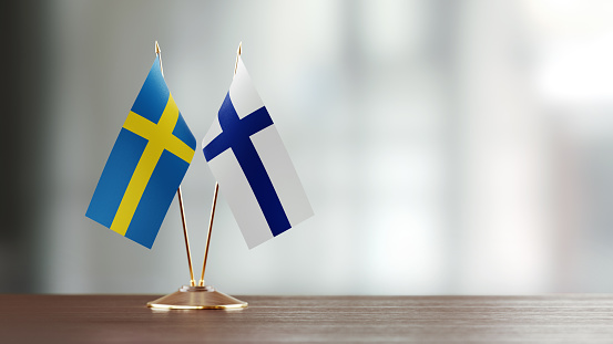 Swedish and Finnish flag pair on desk over defocused background. Horizontal composition with copy space and selective focus.
