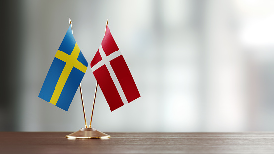 Swedish and Danish flag pair on desk over defocused background. Horizontal composition with copy space and selective focus.