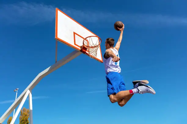 Young Basketball street player making slam dunk.