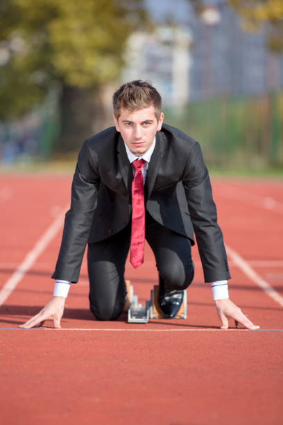 бизнесмен в костюме начинает и готовится к запуску на конкурсе беговой трассы - starting line running sprinting alertness стоковые фото и изображения