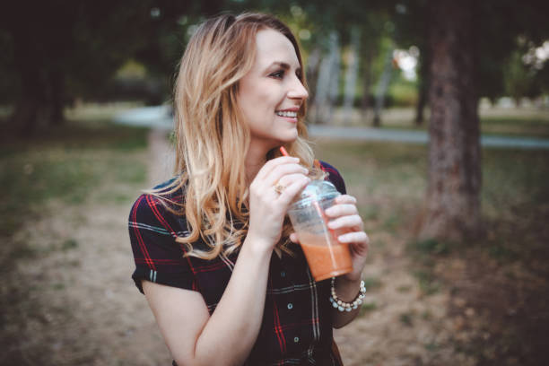 istock Smiling young woman drinking smoothie in the public park 931543528