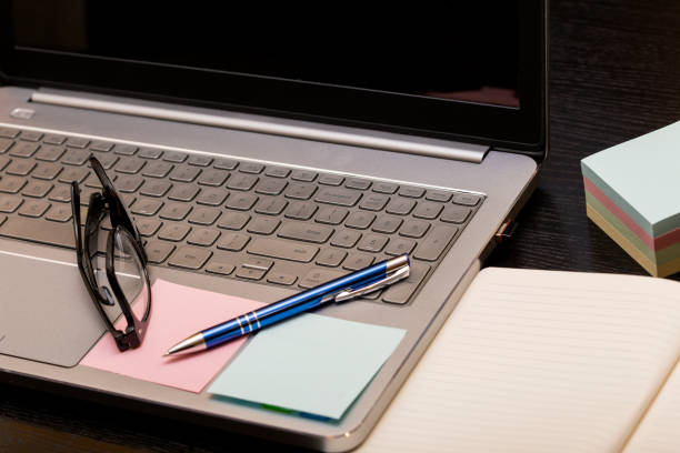 istock Working space with grey laptop computer, glasses on keyboard and pen on open book on black table 931547134