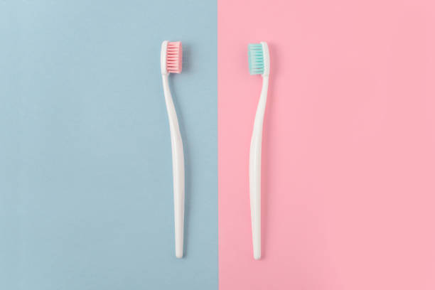 nahaufnahme von zwei kunststoff weiß zahnbürsten mit rosa und blauen borsten auf rosa und blauen hintergrund. kostenloses exemplar raum. - toothbrush pink turquoise blue stock-fotos und bilder