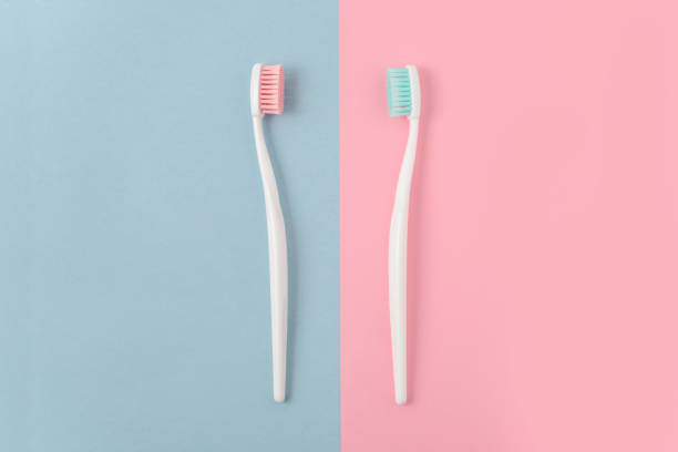 zbliżenie dwóch plastikowych białych szczoteczek do zębów z różowym i niebieskim włosiem na różowym i niebieskim tle. wolne miejsce na kopiowanie. - toothbrush pink turquoise blue zdjęcia i obrazy z banku zdjęć