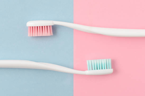 nahaufnahme von zwei kunststoff weiß zahnbürsten mit rosa und blauen borsten auf rosa und blauen hintergrund. kostenloses exemplar raum. - toothbrush pink turquoise blue stock-fotos und bilder