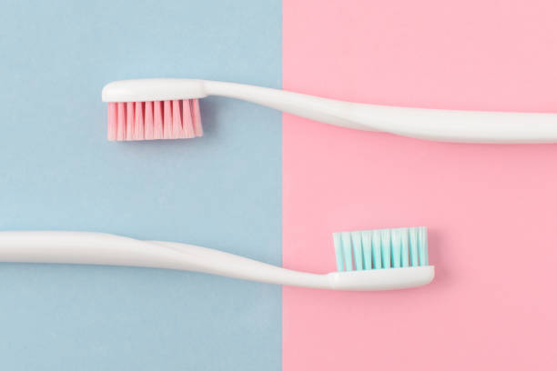 zbliżenie dwóch plastikowych białych szczoteczek do zębów z różowym i niebieskim włosiem na różowym i niebieskim tle. wolne miejsce na kopiowanie. - toothbrush pink turquoise blue zdjęcia i obrazy z banku zdjęć