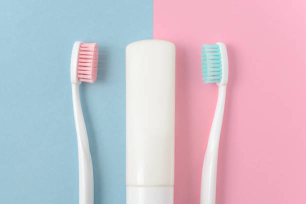 perto de duas escovas de dente brancas plásticas com cerdas rosa e azul e pasta de dentes sobre fundo azul e rosa. espaço de cópia gratuita. - toothbrush pink turquoise blue - fotografias e filmes do acervo