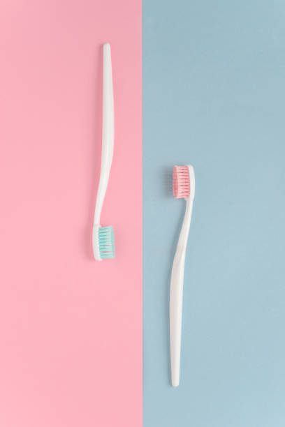 nahaufnahme von zwei kunststoff weiß zahnbürsten mit rosa und blauen borsten auf rosa und blauen hintergrund. kostenloses exemplar raum. - toothbrush pink turquoise blue stock-fotos und bilder