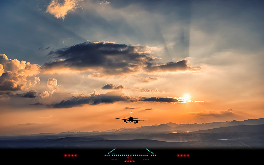 Silhouette of airplane landing to airport runway with beautiful sunset light