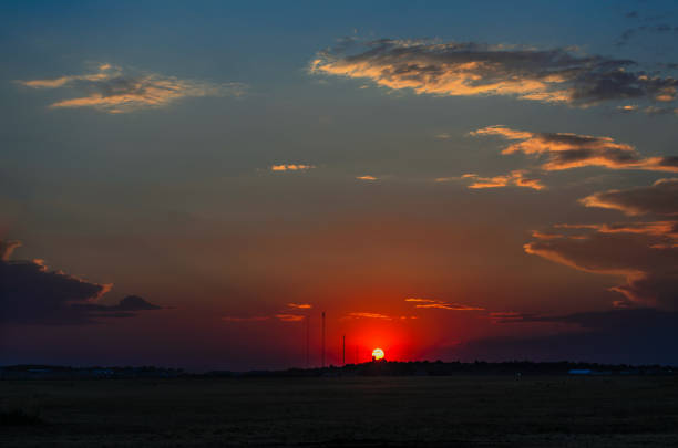 A crimson red sunset over the hill with a black silhouette of an ancient tower and building, a green field in the foreground and a huge blue sky with orange clouds