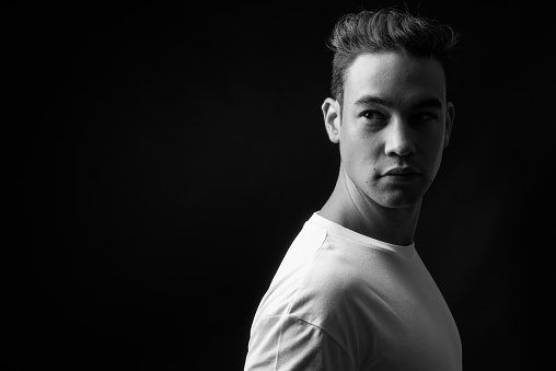 Studio shot of young handsome multi-ethnic man against black background in black and white