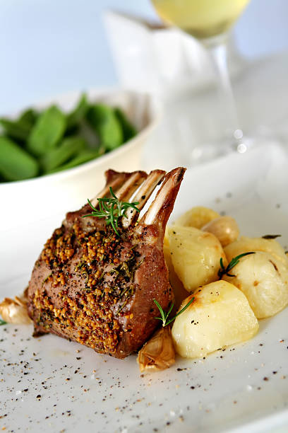 Seasoned rack of lamb served with a side dish Rack of Lamb with rosemary and mustard, and garlic roast potatoes.  rack of lamb stock pictures, royalty-free photos & images
