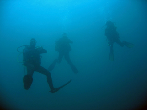 Underwater shot of three male scuba divers exploring huge ship wreck on the sea bottom