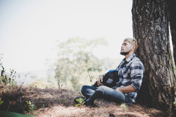 istock Portrait of young beard man sitting alone by a tree with backpack looking away enjoy with nature. 931578958