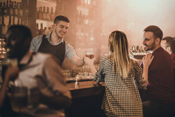 Happy bartender serving his customers with beer in a pub. Young happy bartender serving beer to his customers in a bar. pub bar counter bar men stock pictures, royalty-free photos & images
