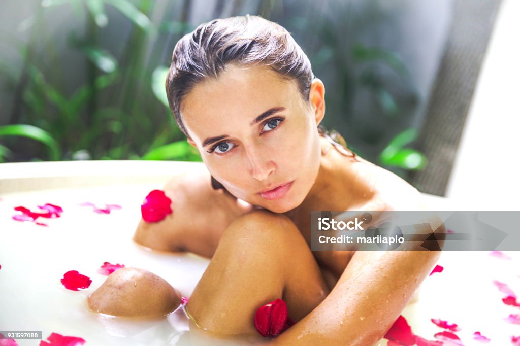Attractive girl takes milk bath with milk and rose petals. Attractive girl takes milk bath and rose petals. Spa treatments for skin. It is on open bath in spa salon Bathtub Stock Photo