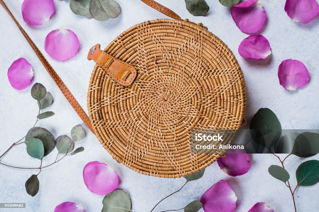 Fashionable rattan bag, flowers rose petals and eucalyptus leaves on light background. Copy space, top view Bag Stock Photo