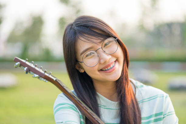 Asian teen girls  with a guitar at the shoulder in the lawn. She is wearing braces  and wear eyeglasses. stock photo