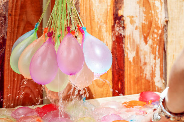 hand holds red water balloon against the summer sun, water bomb ready for cooling down attack.