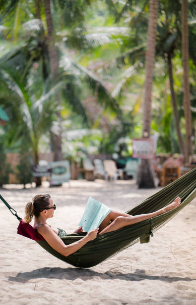 istock Relaxed woman sunbathing in hammock on the beach and reading a book. 931612570