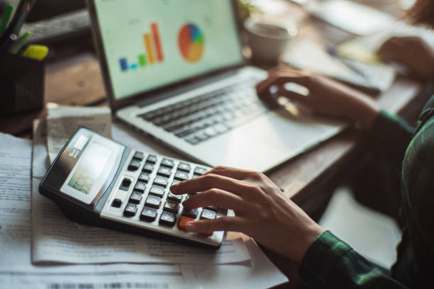 mujer es calcular el costo de la factura. ella está presionando la calculadora. - mano de la mujer escribiendo matemáticas los cálculos se fotografías e imágenes de stock