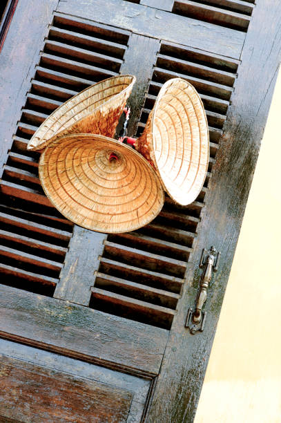 Vietnamese Conical Vietnamese Hats, Hoi An, can be seen hanging against a slatted wooden shuttered window.