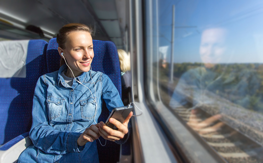 Young woman traveling by train listening music wearing earphones