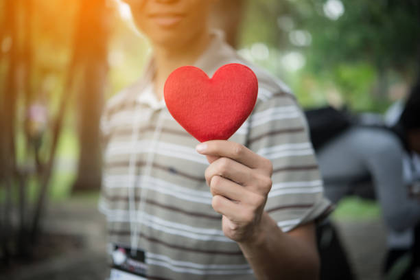 istock Young man holding heart shaped valentine card and looking while standing in the park. 931650182