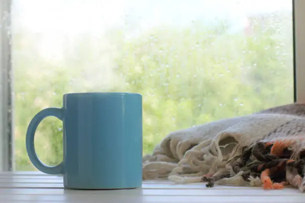 Big blue mug on the table with a blanket against the window with rain drops
