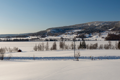 Snowy field with a crossing road and mountain and blue sky in background, picture from Northern Sweden.