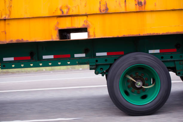 Yellow rusty container on flat bed semi trailer with green wheels on green trailer frame driving on the multiline road