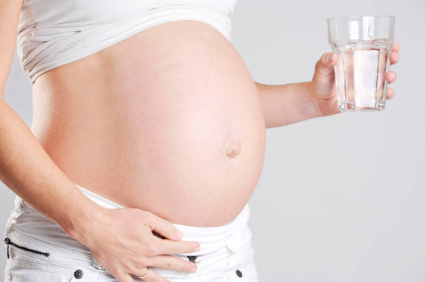 Pregnant woman is holding a glass of water. stock photo