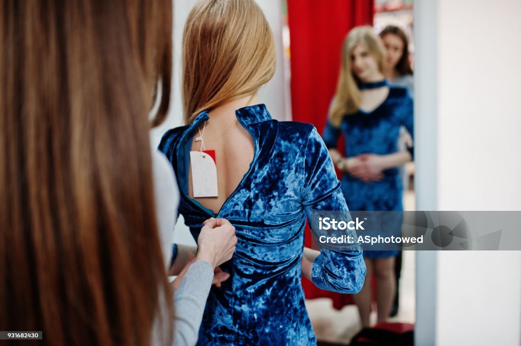 Girl in the mall. Sales consultant helps to dress the dress for buyer at boutique. Adult Stock Photo