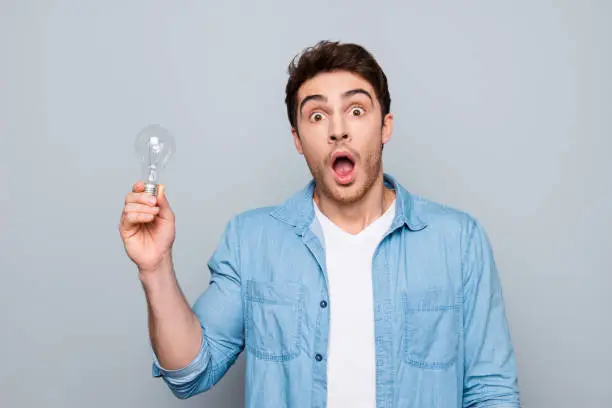 Photo of Portrait of astonished, brunet, caucasian, smart, clever, shocked guy with wide open mouth and eyes having illumination in arm, looking at camera, isolated on grey background