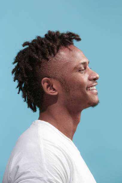 el hombre afroamericano de negocios feliz de pie y sonriendo contra el fondo azul. vista de perfil - perfil vista de costado fotografías e imágenes de stock