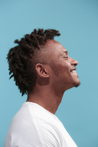 Happy business Afro-American man standing and smiling isolated on blue studio background. African American male profile portrait. Young emotional man. The human emotions, facial expression concept.