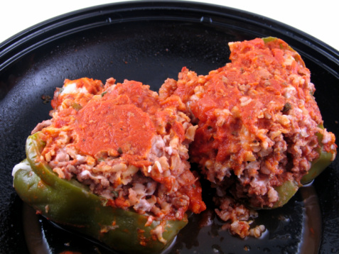 Homemade baked red bell peppers with spicy minced meat filling and tomato sauce. Served with cross section view on a plate on kitchen table background.
