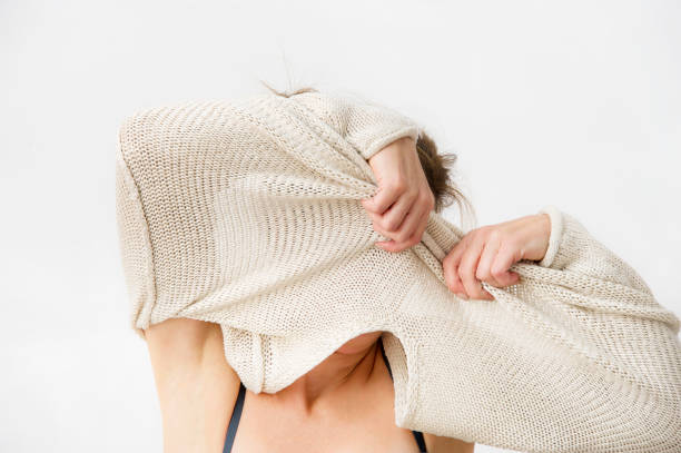 Young woman is taking off her sweater, covering her face. stock photo